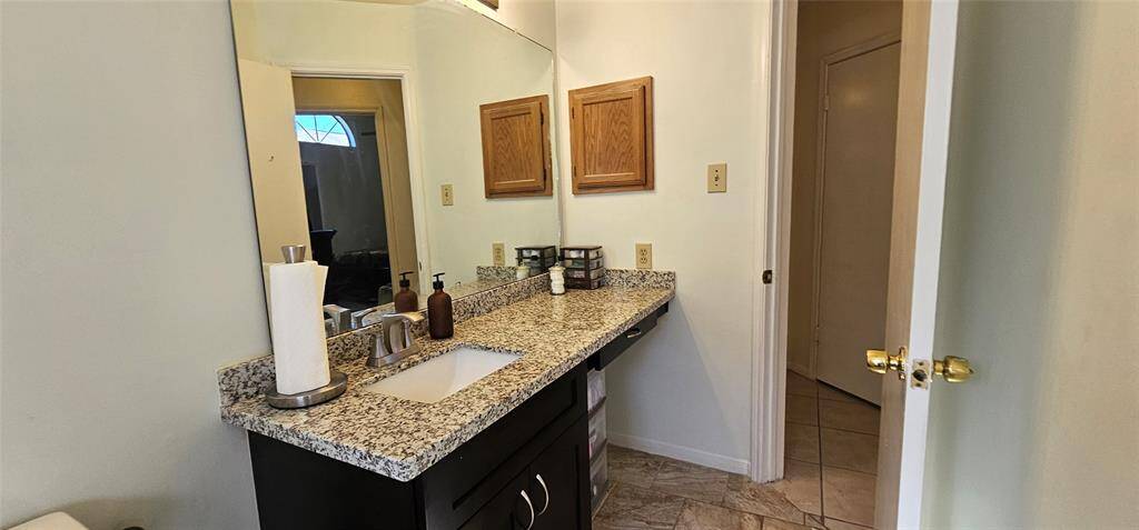 2nd bathroom features a granite countertop with a single sink, medicine cabinet,  a large mirror, and ample storage space.