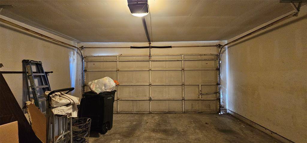 Spacious two-car garage. There's some storage along the back of the garage, including a ladder and bins, providing potential for organization and utility.