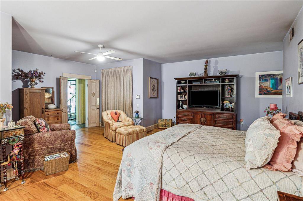 Primary bedroom with hardwood floors, ceiling fan with light, and a sitting area.