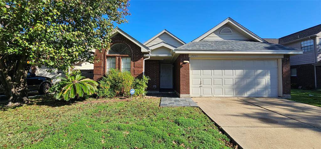 Charming brick home with a well-maintained front yard, featuring a lush lawn and mature tree. The house includes a two-car garage and a welcoming entrance with a gabled roof.
