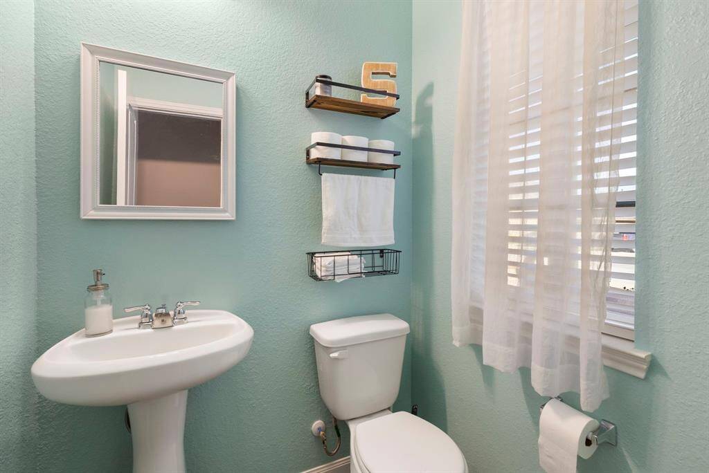 The half bath with pedestal sink and decorative mirror is located just off the foyer.