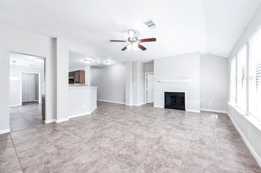 Expansive living space featuring a cozy fireplace, ample natural light, and ceiling fan.