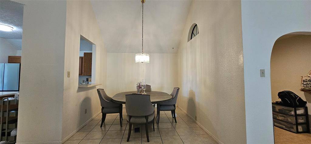 Dining area has tiled flooring and a vaulted ceiling with chandelier. An open window connects to the kitchen for convenient serving.