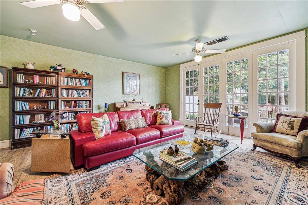 Living room with hardwood floors, ceiling fans with lights, and doors to the lush, green side yard.