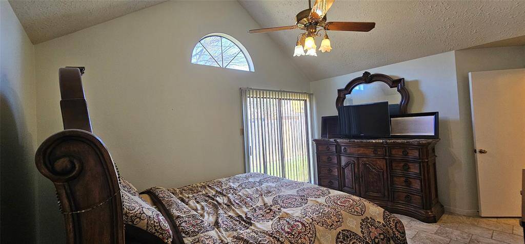 Primary bedroom features high vaulted ceilings, a large arched window for natural light and a ceiling fan.