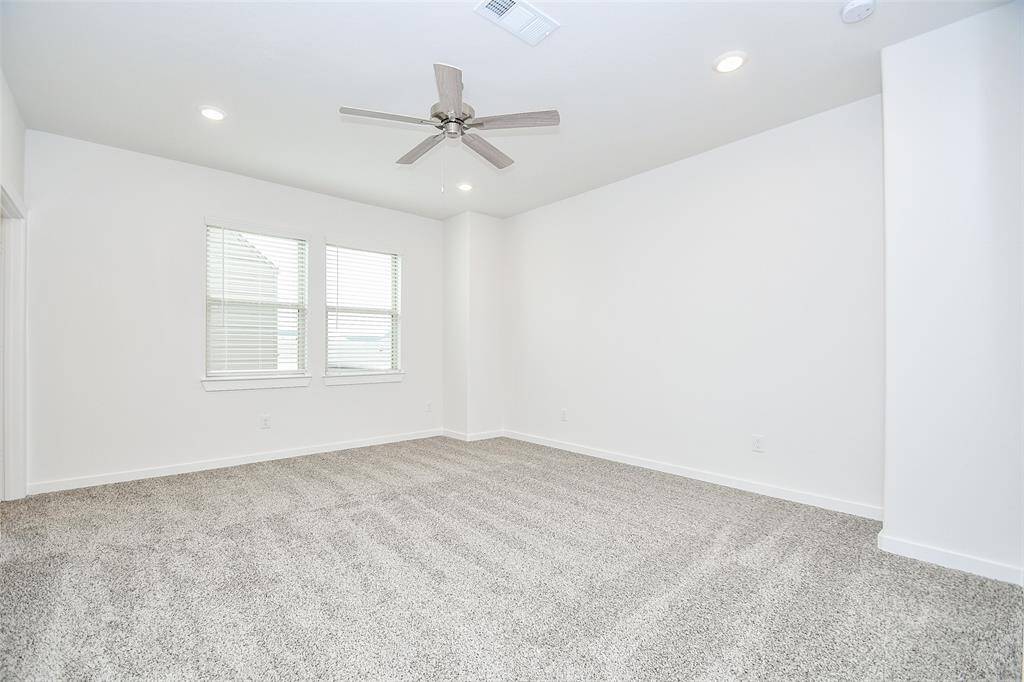 The primary bedroom. A serene retreat, carpeted in a soft, neutral tone and featuring a ceiling fan for added comfort. Its spacious layout offers a welcoming atmosphere for relaxation.