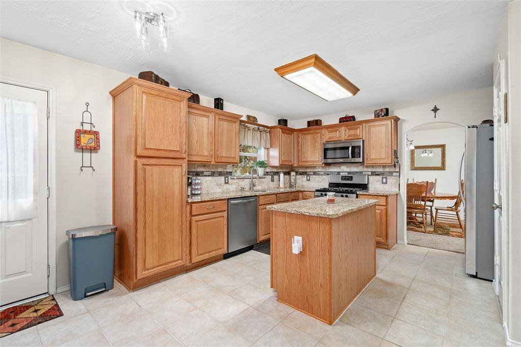 Your bright, well-maintained kitchen features natural wood cabinetry, modern appliances, granite counter tops, a central island, tile flooring, and over the sink window.
