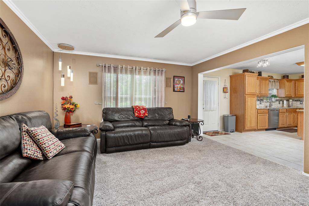 Your new living room is well-lit with a combination of natural light from the window and a modern ceiling fan and corner pendant light fixture. The open floor plan leads into a kitchen providing a seamless transition for entertaining and daily living.