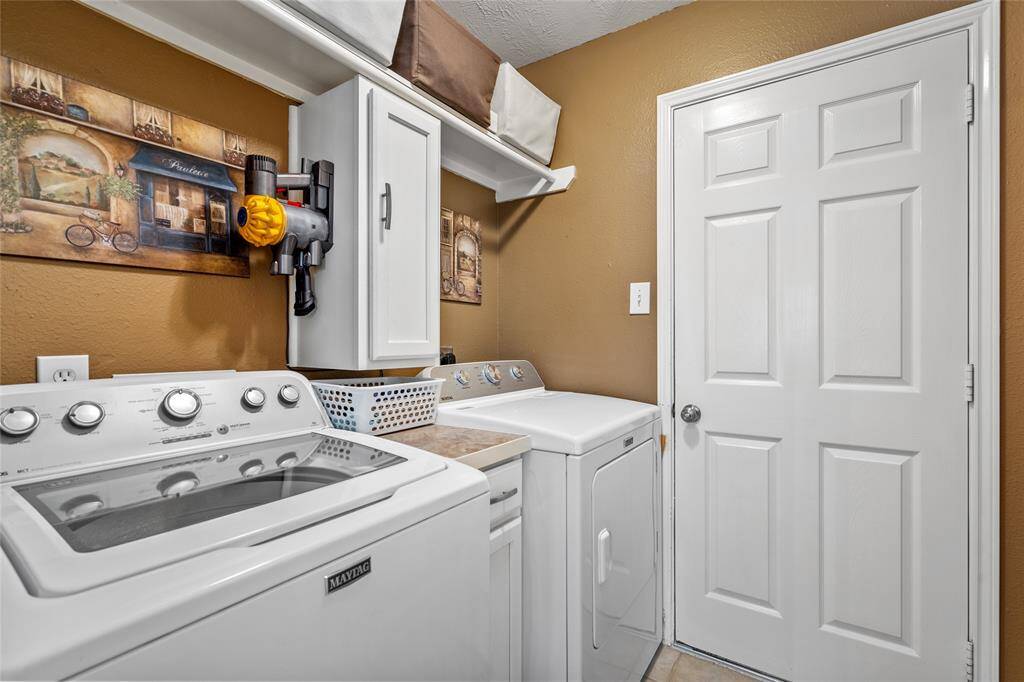 Your tidy laundry room has ample storage with overhead shelving, and a wall-mounted cabinet. The room is finished with a warm color scheme creating a cozy ambiance.