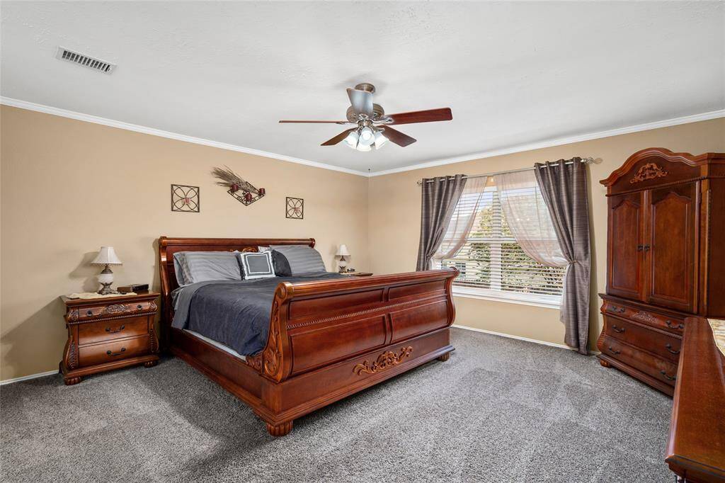 Your spacious primary bedroom has a ceiling fan, large window, neutral wall colors and carpeted flooring.