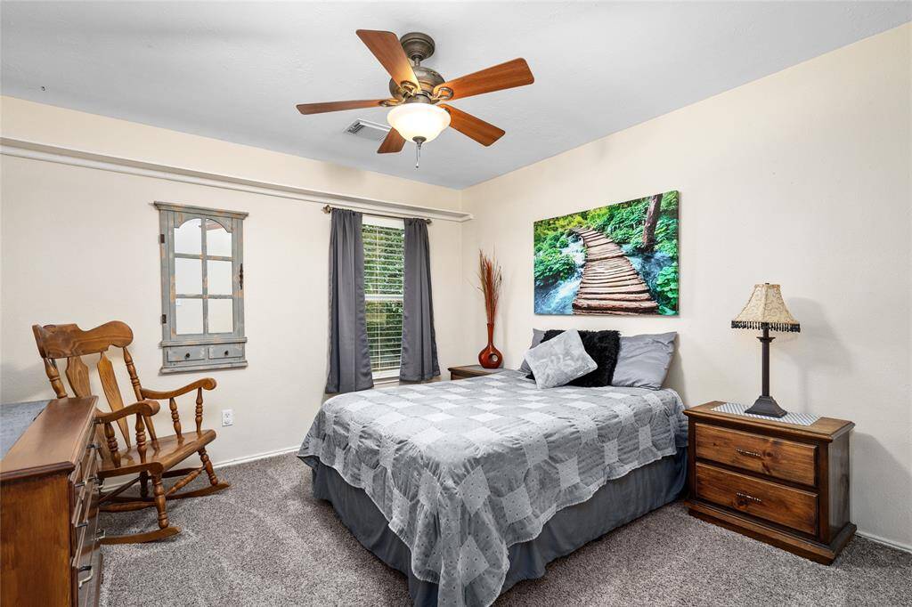 Another secondary bedroom has carpeted flooring, light-colored walls, a ceiling fan with lighting and a window creating a comfortable and inviting space.