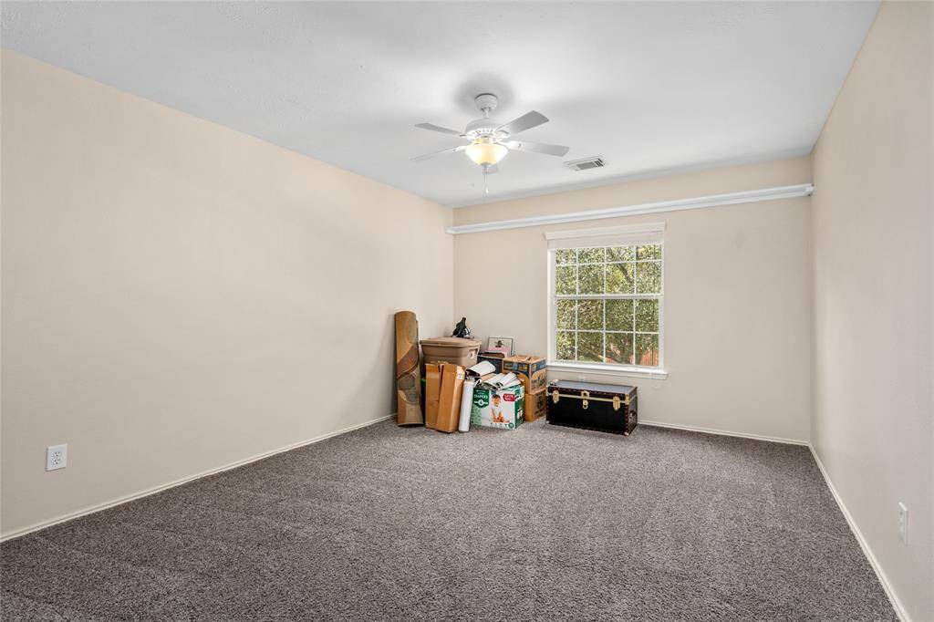 Another bedroom with neutral walls and carpet flooring, featuring a ceiling fan and a large window that allows for plenty of natural light.
