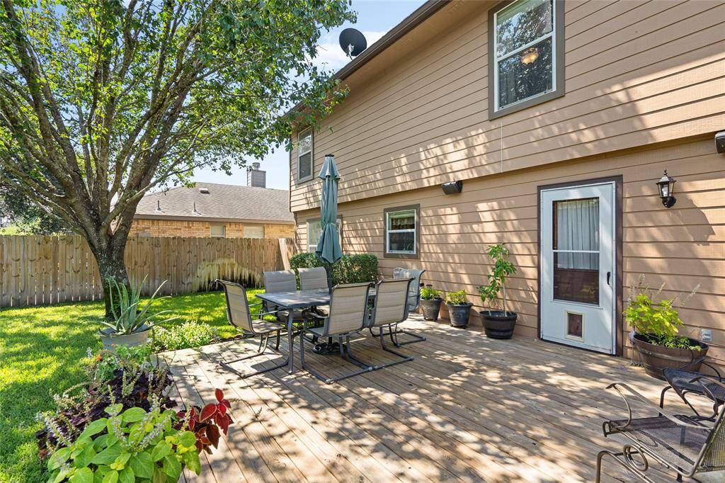 Your wooden deck and and shade tree are perfect for outdoor dining and relaxation. The area is complemented by a well-maintained lawn and privacy fence, offering a serene outdoor extension to the home.
