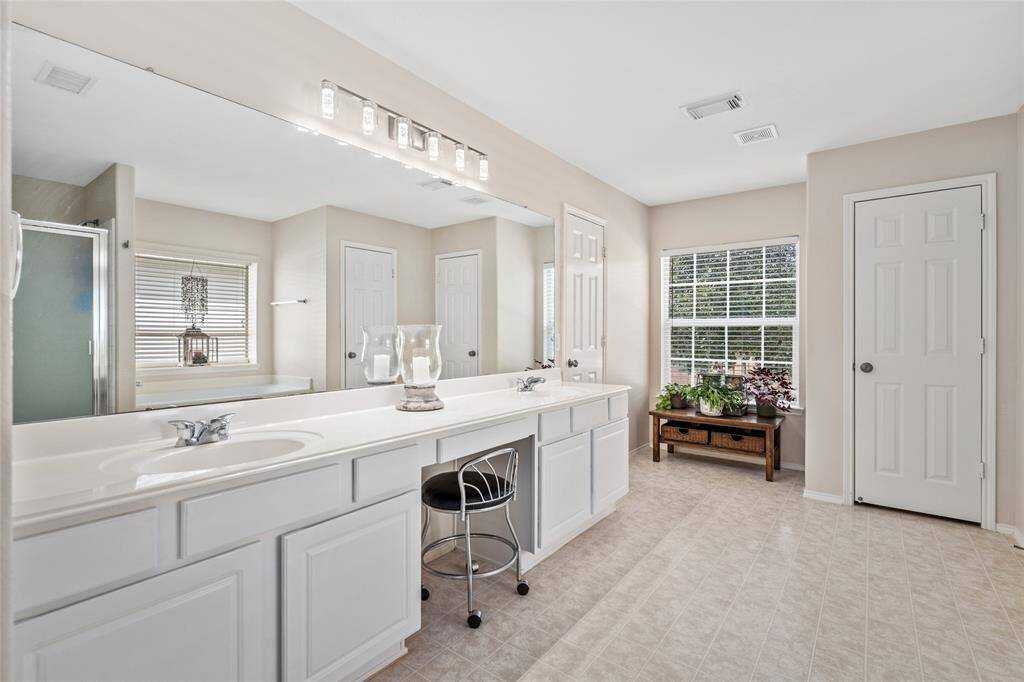Your luxurious, well-lit primary bathroom includes a large vanity with dual sinks, ample cabinetry, a full-width mirror with modern lighting. A window provides natural light, and there's a cozy nook by the window.