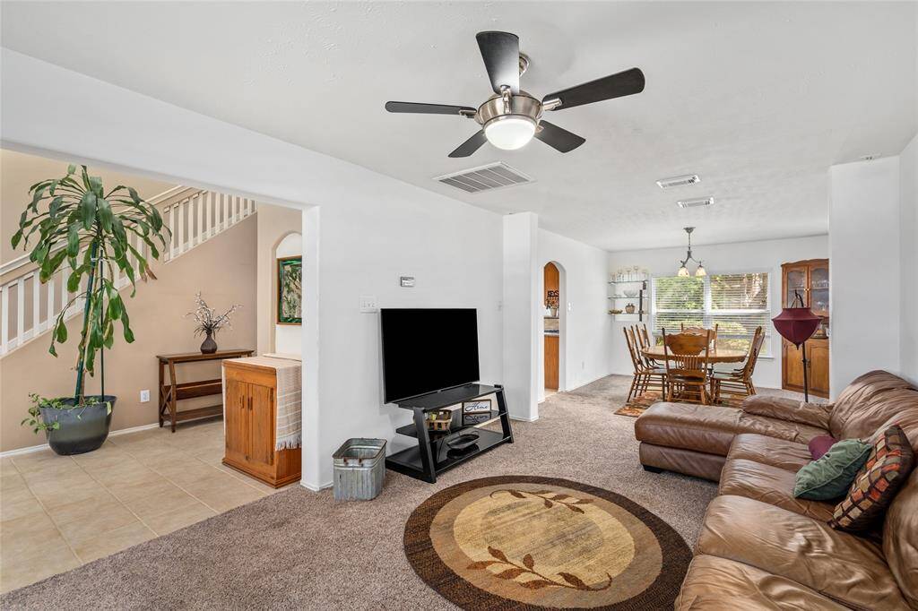 Your family room has a bright, open-concept that is open to the entry and dining areas. The room features carpeting, a modern fan, and ample natural light. The space is complemented by neutral tones, giving it a warm and inviting atmosphere.