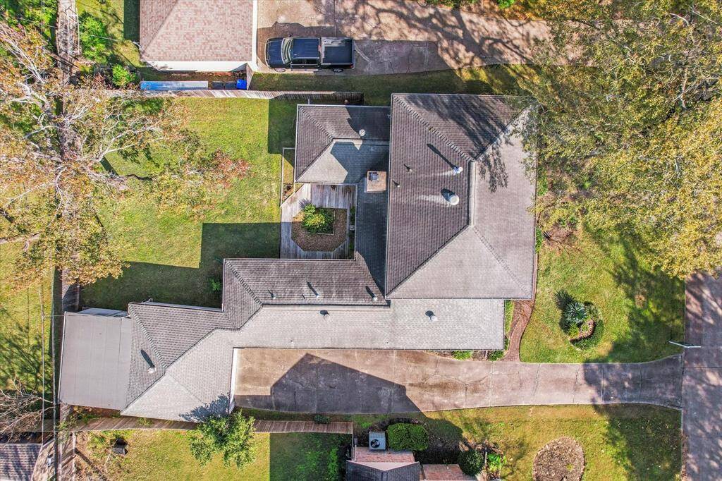 This aerial photo shows a spacious property with a well-maintained, multi-section roof. It features a large, grassy backyard with mature trees and landscaped areas. The driveway leads to an attached garage, and the overall layout provides ample outdoor space.