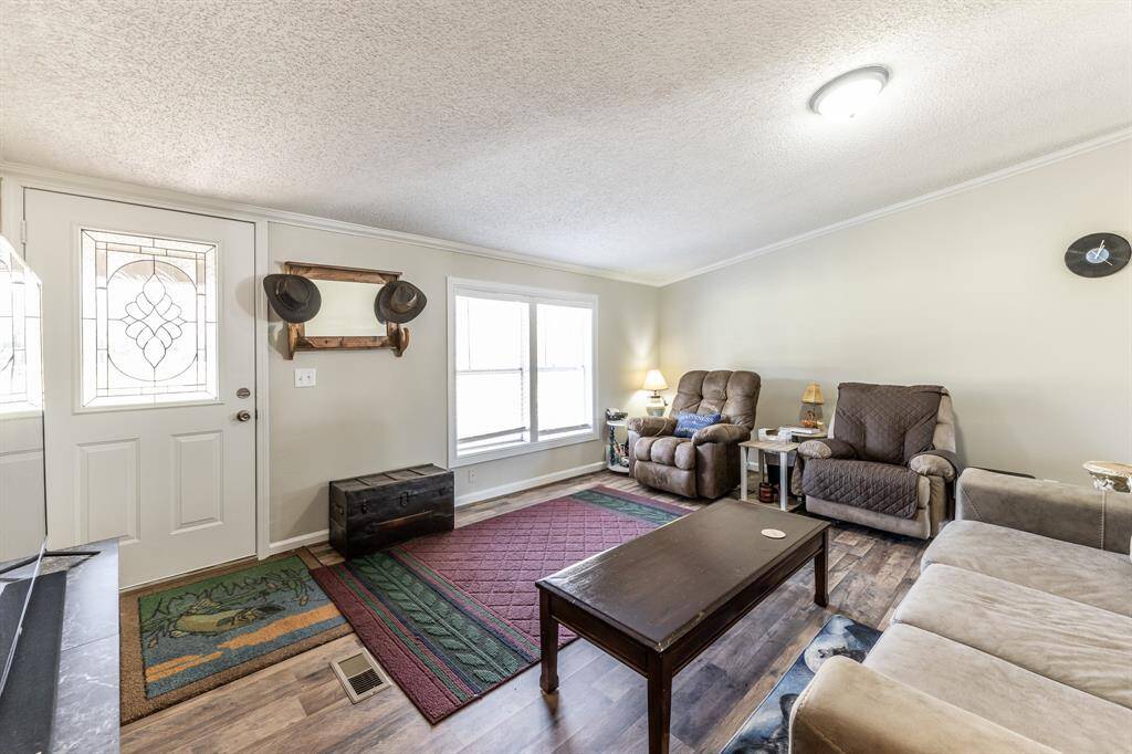 Cozy living room with natural light, featuring comfortable seating, a patterned rug, and a welcoming atmosphere. The entry door has decorative glass, and the space includes a practical layout with a mix of modern and rustic accents.