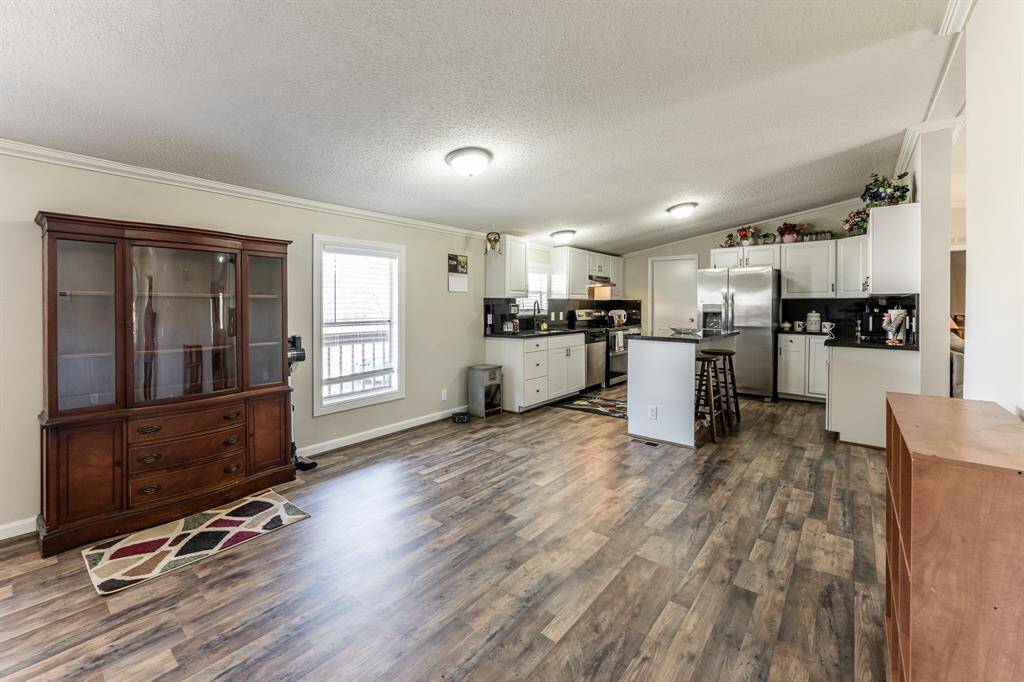 This photo showcases a spacious, open-concept kitchen and dining area with wood flooring, white cabinetry, and modern appliances. It features a central island with seating and ample natural light from a large window, creating a warm and inviting atmosphere.