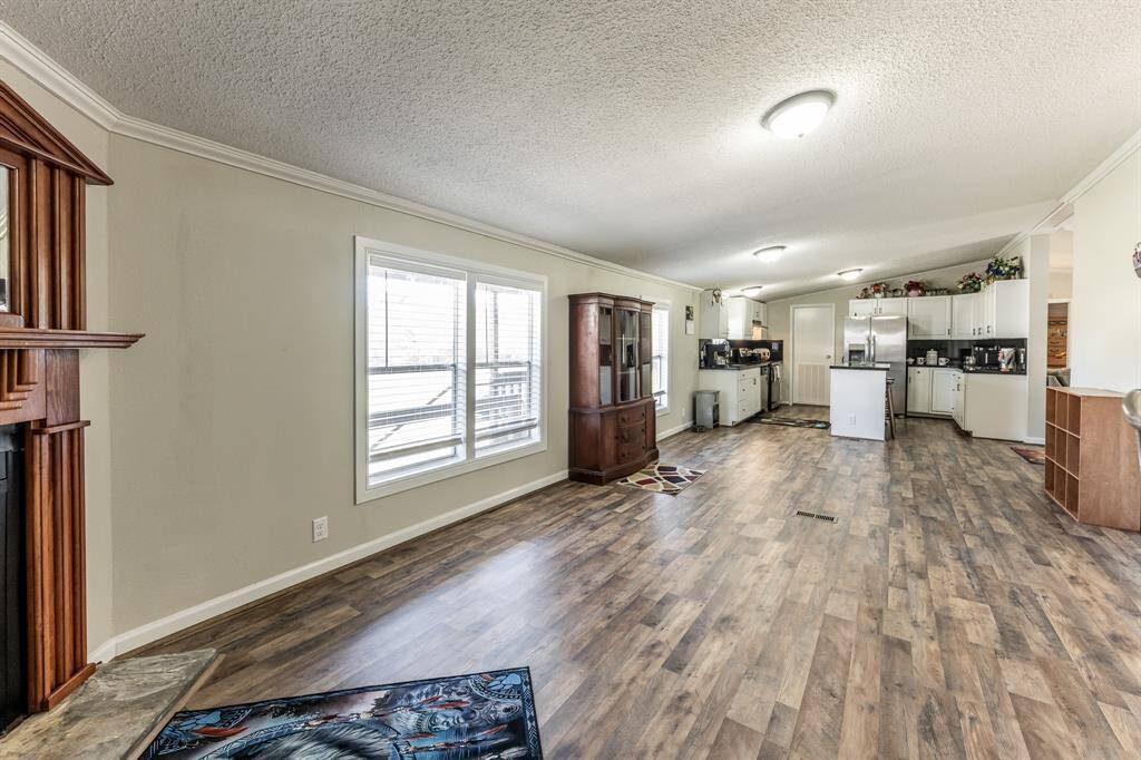 This spacious open-concept living area features wood-style flooring, ample natural light from large windows, and a cozy corner fireplace. The kitchen is modern with white cabinetry and stainless steel appliances, perfect for entertaining.