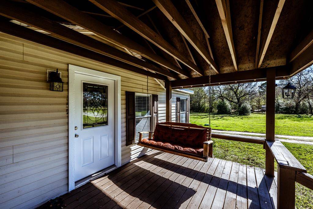 Charming covered porch with a wooden swing, perfect for relaxing and enjoying the scenic view of the lush green yard. A welcoming entryway with a decorative glass door adds character to the home.