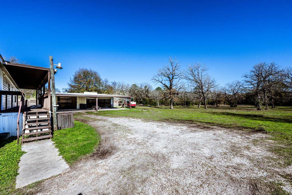 A rural property with a spacious yard, featuring a wooden porch and a large garage. Surrounded by trees, it's ideal for those seeking tranquility and outdoor space.