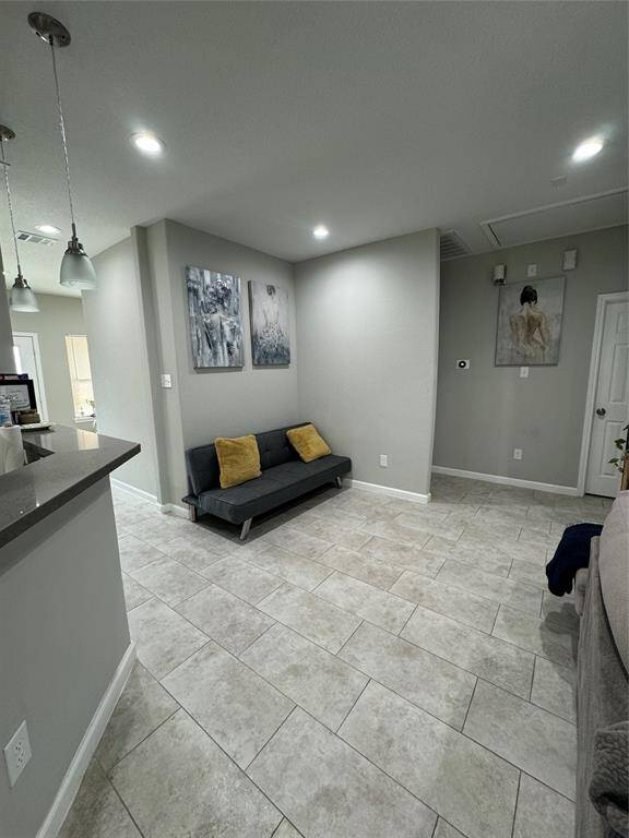 This photo showcases a modern living area with light gray tile flooring and neutral walls. It features recessed lighting, creating an open and inviting atmosphere.