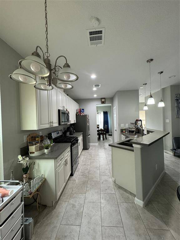 This photo shows a modern kitchen with white cabinets, stainless steel appliances, and tiled flooring. It features a spacious layout with ample counter space and overhead lighting, offering a bright and functional cooking area.
