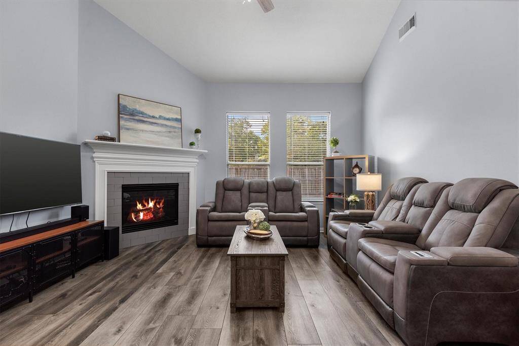 This is a cozy and modern living room featuring high ceilings, large windows for natural light, a stylish fireplace, comfortable seating, and wood-look flooring, creating an inviting atmosphere ideal for relaxation and entertainment.