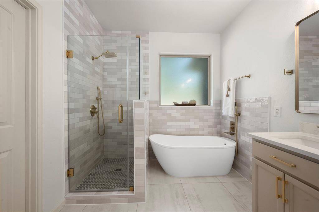The luxurious primary bathroom features a frameless glass shower with sleek tile work, a freestanding soaking tub, and gold fixtures for a modern touch.