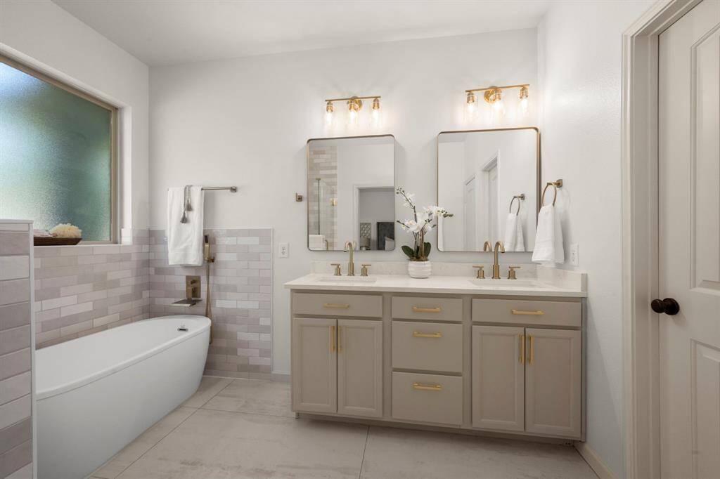 The primary bathroom boasts a double vanity with sleek quartz countertops, gold accents, and framed mirrors.