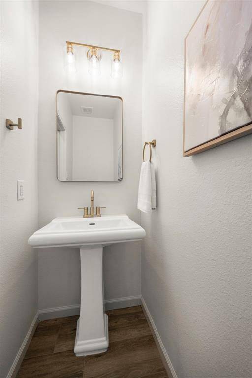 The half bath features a pedestal sink, gold accents, and a modern light fixture that elevates the space.