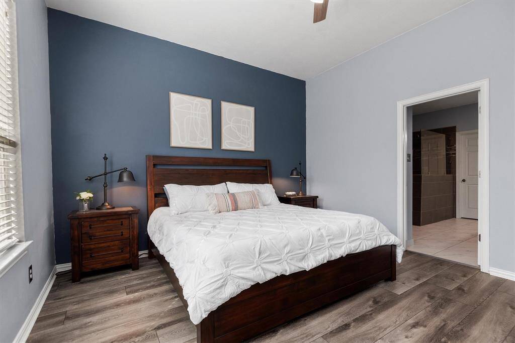 This is a cozy bedroom with a stylish dark blue accent wall, complemented by a lighter blue on the other walls. The room has vinyl wood flooring and provides access to an en-suite bathroom.