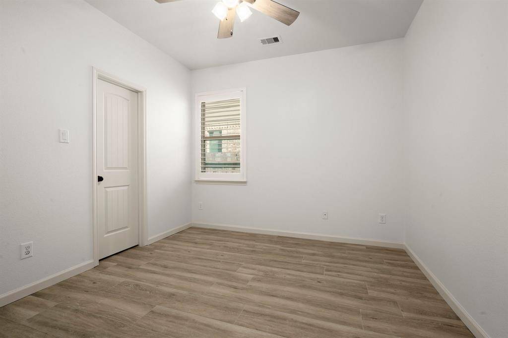 This secondary bedroom offers a cozy yet functional space with modern wood-look flooring, a ceiling fan, and a large window for natural light.