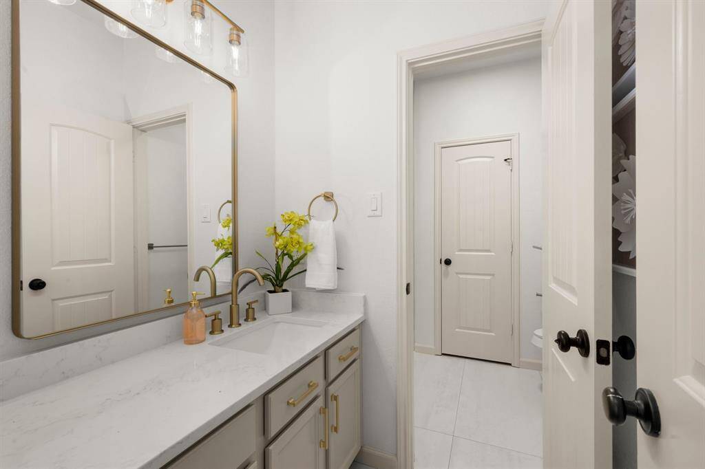 This stylish full bathroom features a sleek quartz countertop, gold fixtures, and a spacious vanity with ample storage.