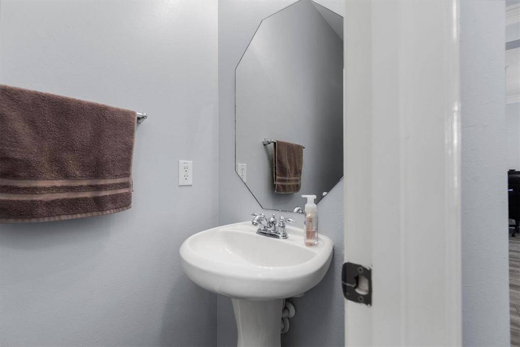 This is a half-bath featuring a pedestal sink, an octagonal mirror, and fresh, light blue walls. It's well-suited for guest use or as an additional bathroom in the home.