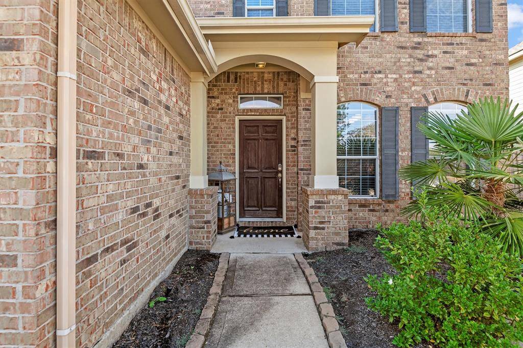 This is a welcoming entrance to a two-story brick home featuring a dark wood front door with sidelights, arched transom window, covered entryway, and landscaped garden beds.