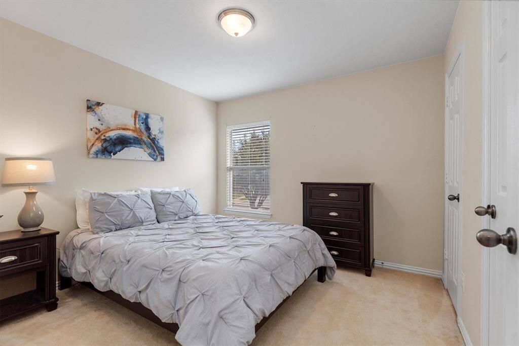 This is a well-lit, cozy bedroom featuring neutral walls, a large window, plush carpeting, and tasteful decor.