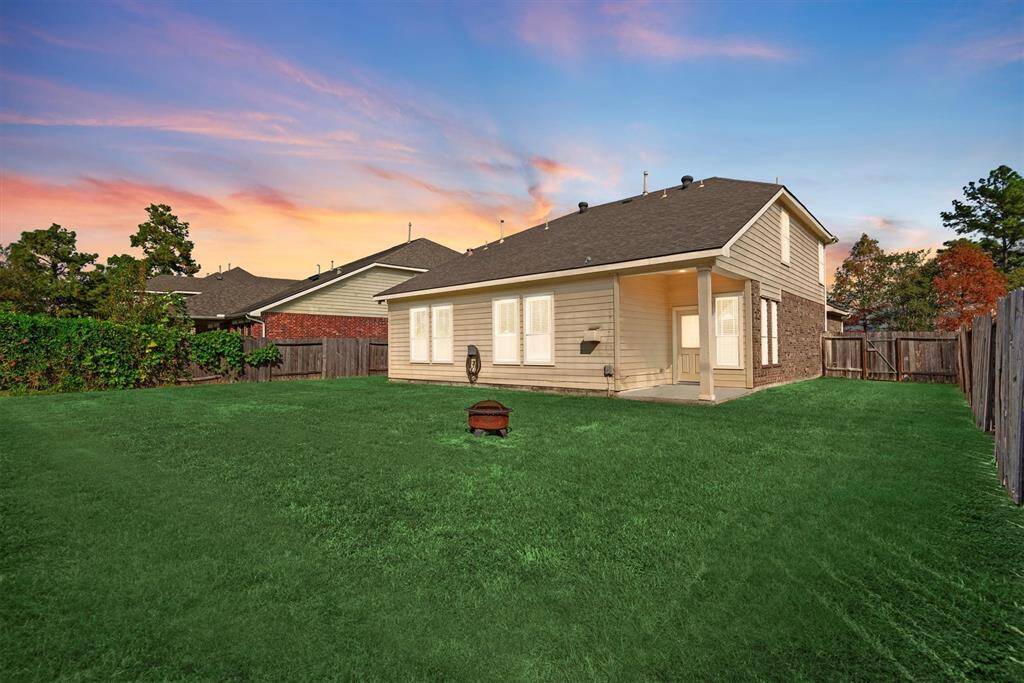 This image showcases the backyard of a single-family home at dusk, featuring a well-maintained lawn, a cozy patio area, and a wooden privacy fence. The home's exterior is finished in a neutral siding with brick accents.
