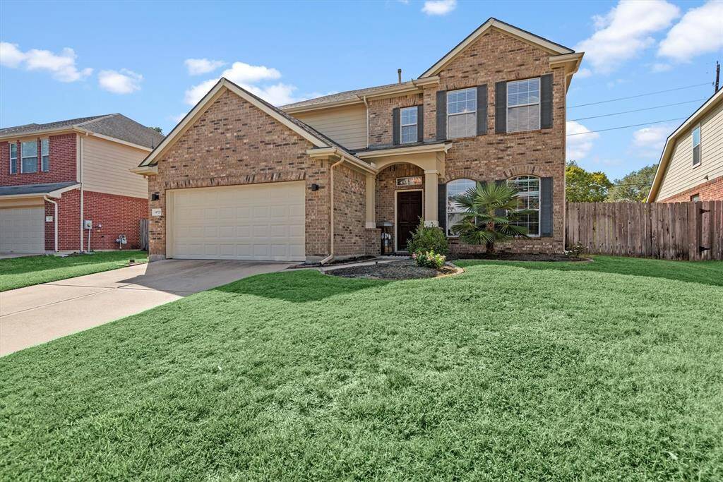 This is a two-story brick home featuring a well-maintained lawn, an attached two-car garage, and a welcoming entrance with a large front window.