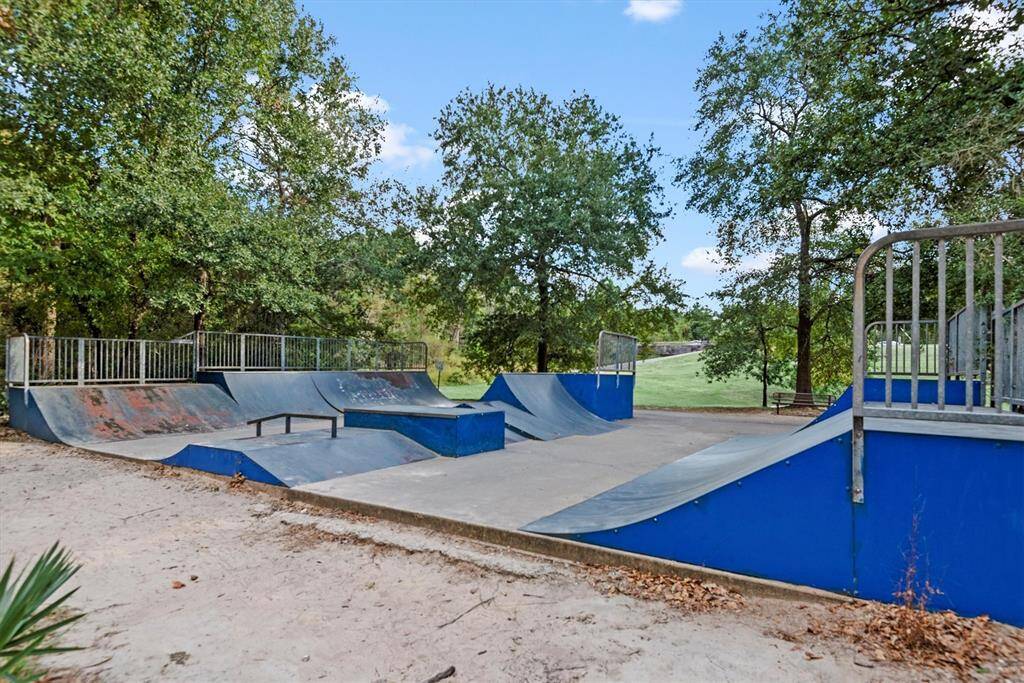 The community skatepark with various ramps and rails, nestled among lush trees, offering a recreational outdoor space for skating enthusiasts.