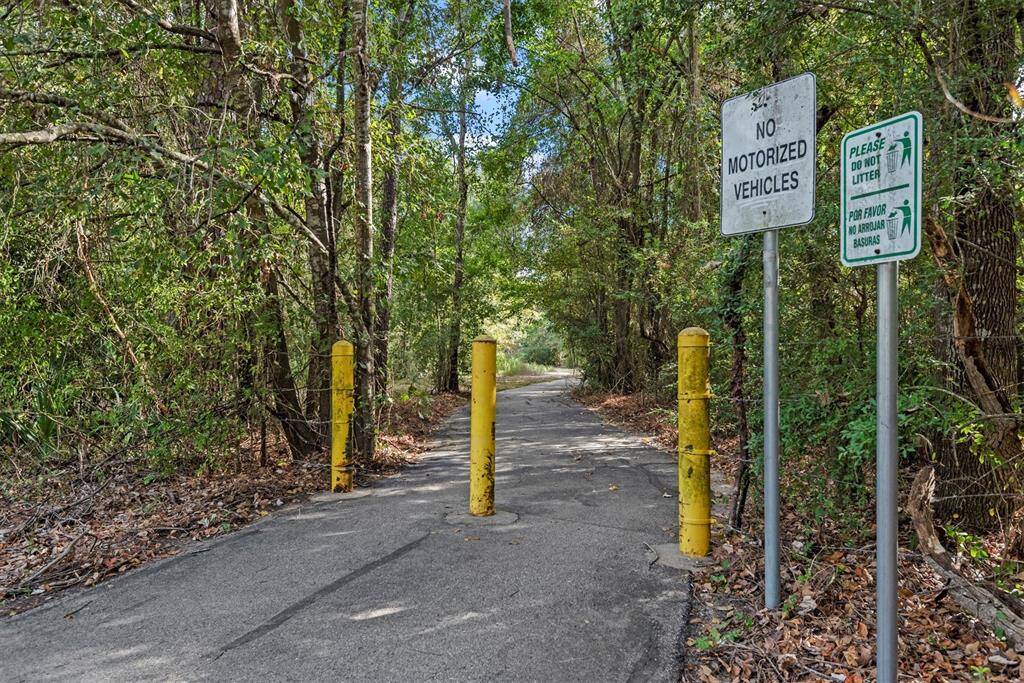 This is a paved pathway surrounded by lush greenery, indicating a serene and natural setting. It's a pedestrian-friendly area with signs indicating no motorized vehicles and a reminder to not litter. It suggests a community-conscious neighborhood with access to walking or biking trails.