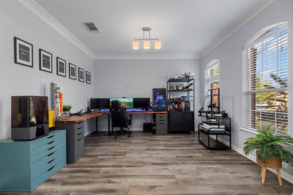 This is a spacious and modern home office with a large corner desk setup, ample natural light from two large windows, and a clean, neutral color scheme.