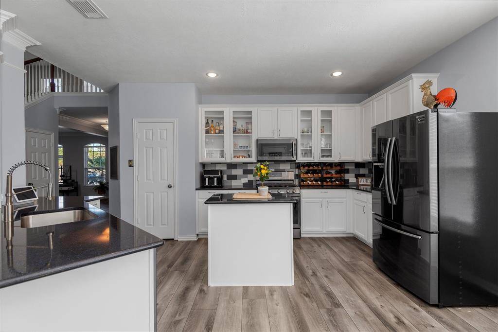 Modern kitchen with white cabinetry, stainless steel appliances, and an island, featuring wood-look flooring and an open layout connecting to the living area.