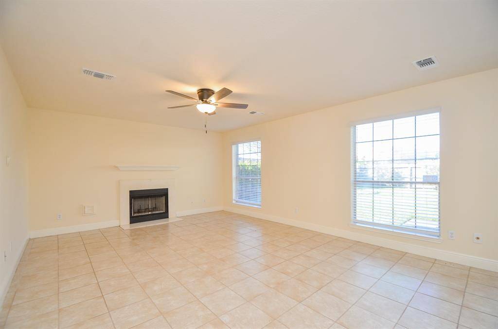 Bright living room with tiled flooring, featuring a cozy fireplace and large windows that let in ample natural light. Ceiling fan adds comfort.