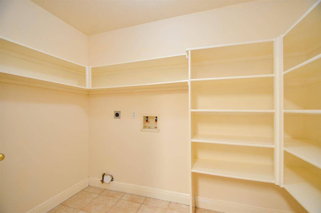 This room features ample built-in Pantry shelving and tile flooring, ideal for use as a laundry or utility room. It includes connections for Washer and Dryer, offering both functionality and storage.