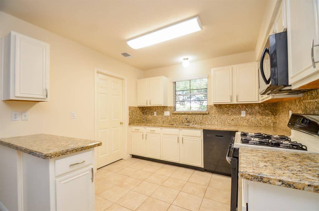Bright kitchen with granite countertops, ample white cabinetry, and modern appliances. Includes a gas stove, dishwasher, and tiled flooring. Cozy and functional with a pleasant window view.