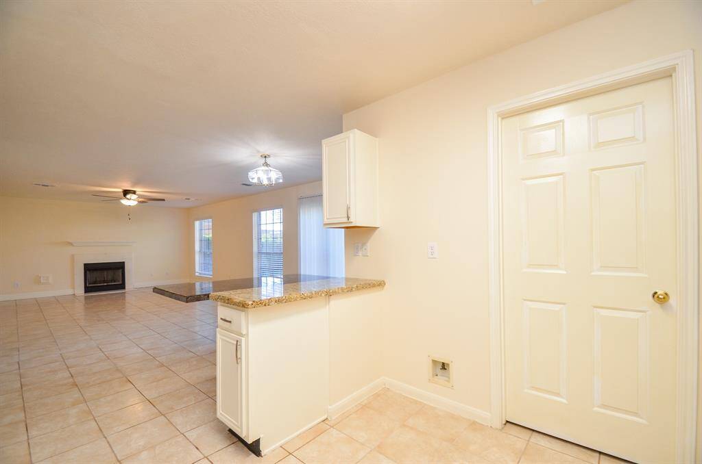Spacious open-plan living area with tiled floors, a cozy fireplace, and ample natural light from large windows. The kitchen features a granite countertop and modern lighting.