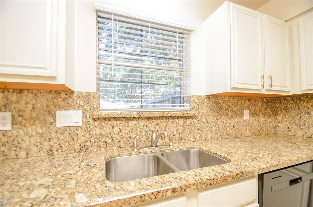 Bright kitchen with granite countertops, stainless steel sink, and white cabinetry, complete with a window offering natural light.