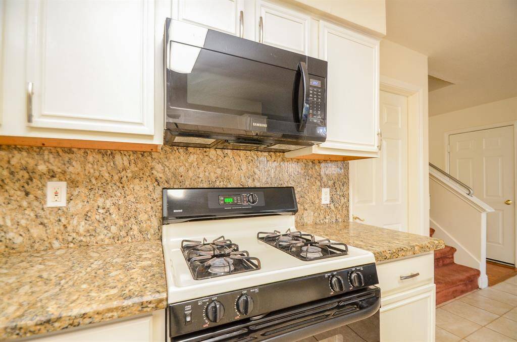 Modern kitchen with granite countertops, gas stove, and built-in microwave. Bright cabinetry enhances the space, and there's easy access to the hallway and stairs.