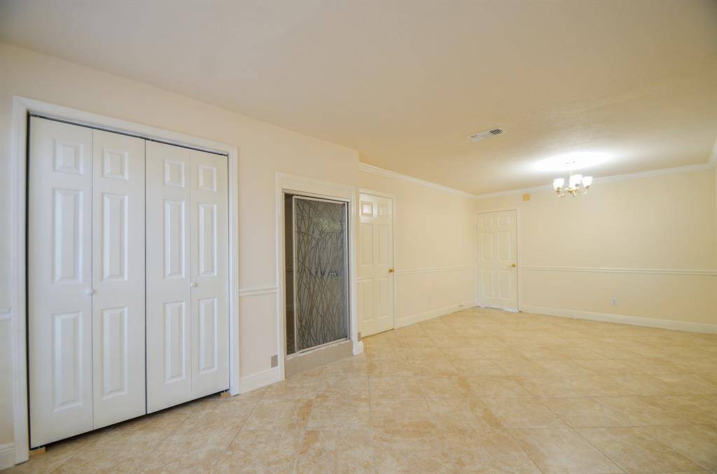 Spacious bedroom on first floor with neutral walls and tile flooring, featuring a chandelier, ample closet space, and a decorative shower glass door.